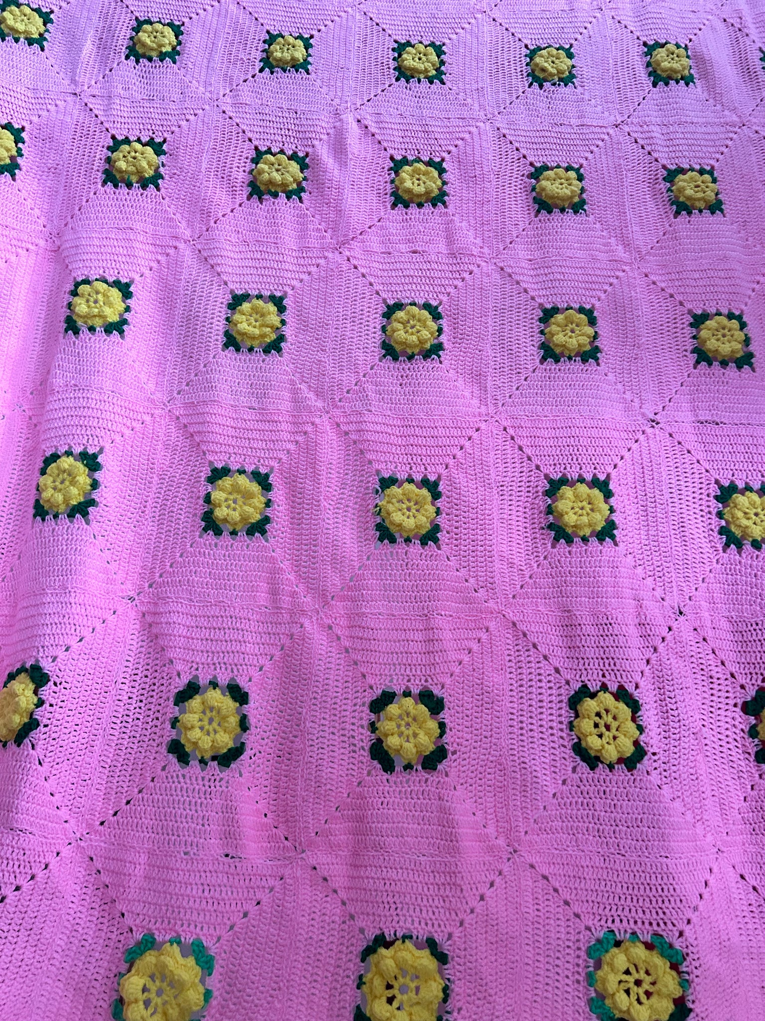 Pink hand knitted blanket with yellow crochet flowers